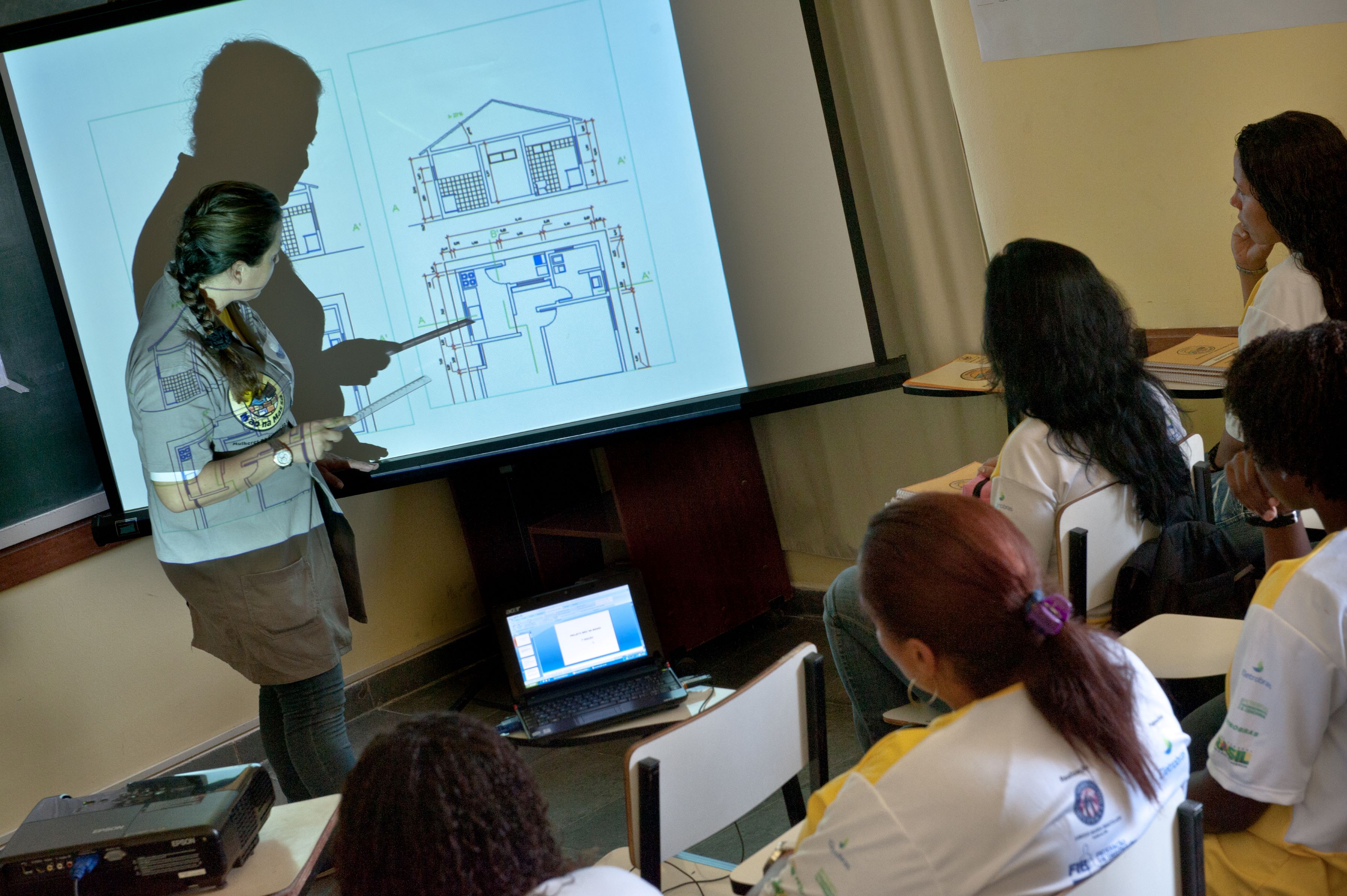 Alunas em sala de aula obervando a professora explicando no quadro